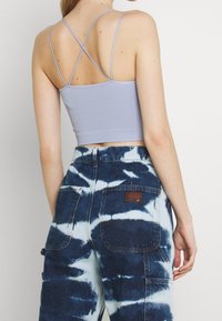 Ljuslila ribbad crop top med tunna korsade axelband, tillsammans med blå batikmönstrade cargobyxor med fickor och etikettdetalj.