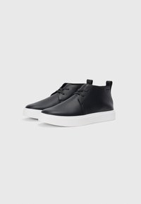 Pantofi din piele neagră cu un finisaj neted, cu talpă din cauciuc alb, un design discret cu siret și o înălțime joasă la gleznă.