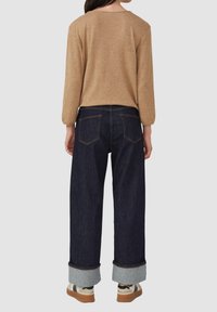 Bruine gebreide top met lange mouwen, gecombineerd met donkerblauwe brede jeans met omgeslagen manchetten en casual sneakers.