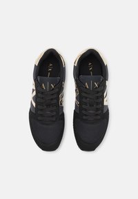 Sneaker sportive nere e beige con dettagli in rete, suede e finiture lucide. Presentano lacci piatti e logo sulla linguetta e sui lati.