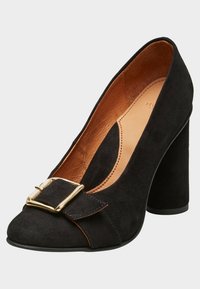 Černá semišová lodička na vysokém podpatku s kulatou špičkou, zdobená zlatou sponou a s hnědým vnitřním podšíváním. Blokový podpatek pro stabilitu.