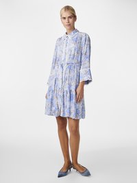 Robe imprimée bleu clair avec un col, des manches longues et des poignets évasés, dotée d'une taille cintrée et d'une jupe superposée. Associée à des talons bleus.