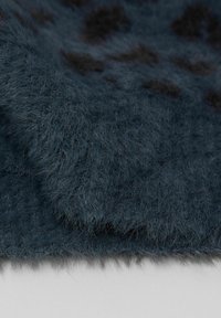 Tkanina ze sztucznego futra w ciemnoniebieskim kolorze o miękkiej, puszystej fakturze z czarnymi plamami. Krawędzie są lekko podwinięte, tworząc warstwowy wygląd.