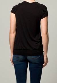 Top nero a maniche corte con dettagli arricciati sulla spalla, in tessuto morbido e vita aderente, abbinato a jeans in denim.