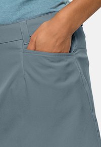 Světle modrá, měkká textilie; detail sukně s boční kapsou, vykazující elegantní design a hladké provedení.