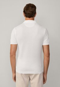 Polo shirt bianco con maniche corte realizzato in tessuto texture, caratterizzato da un colletto e da un design aderente, visto da dietro.