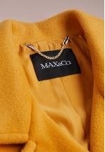 Interno di un cappotto giallo con un'etichetta nera recante il testo "MAX&CO". Un dettaglio in catena argentata collega l'etichetta al tessuto del cappotto. Texture morbida.
