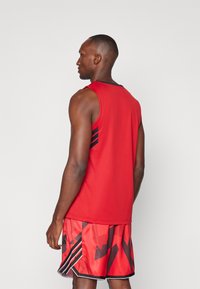 Top deportivo rojo sin mangas con un acento negro en los hombros; combinado con shorts rojos que presentan un patrón geométrico negro y franjas laterales.