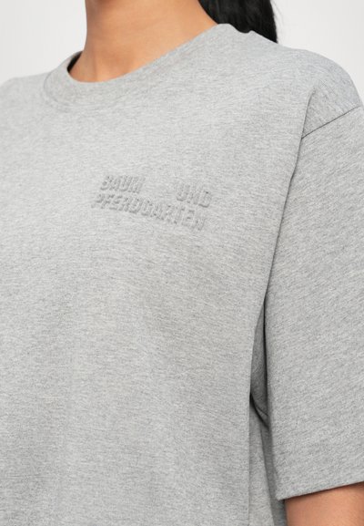 Camiseta de algodón gris con escote redondo, ajuste relajado y mangas cortas. Presenta texto en relieve en el pecho. Textura suave, diseño minimalista.