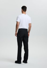 Pantalones negros de corte recto, combinados con una camiseta blanca ajustada. En la parte de atrás hay un pequeño logo en el cuello. El calzado es negro y deportivo.