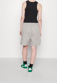 Gray cotton shorts with an elastic waistband, paired with a black sleeveless top and green high-top sneakers, viewed from the back.