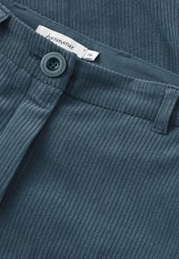 Byxor i anka blå kordflors med en texturerad yta, med en frontknappstängning och en etikett som visar märke och storlek.