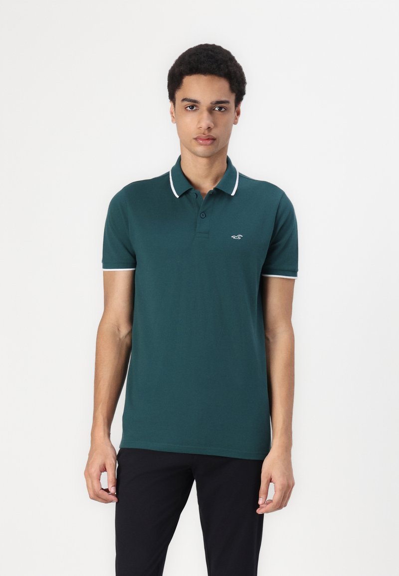 Polo shirt vert en coton avec une coupe slim, présentant un col et un liseré blanc contrastant sur les manches et le col, logo brodé sur la poitrine.