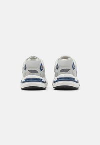 Weiße und graue Sportschuhe mit blauen Akzenten, ausgestattet mit Mesh-Einsätzen und einer gepolsterten Sohle, die für Unterstützung und Komfort ausgelegt sind.