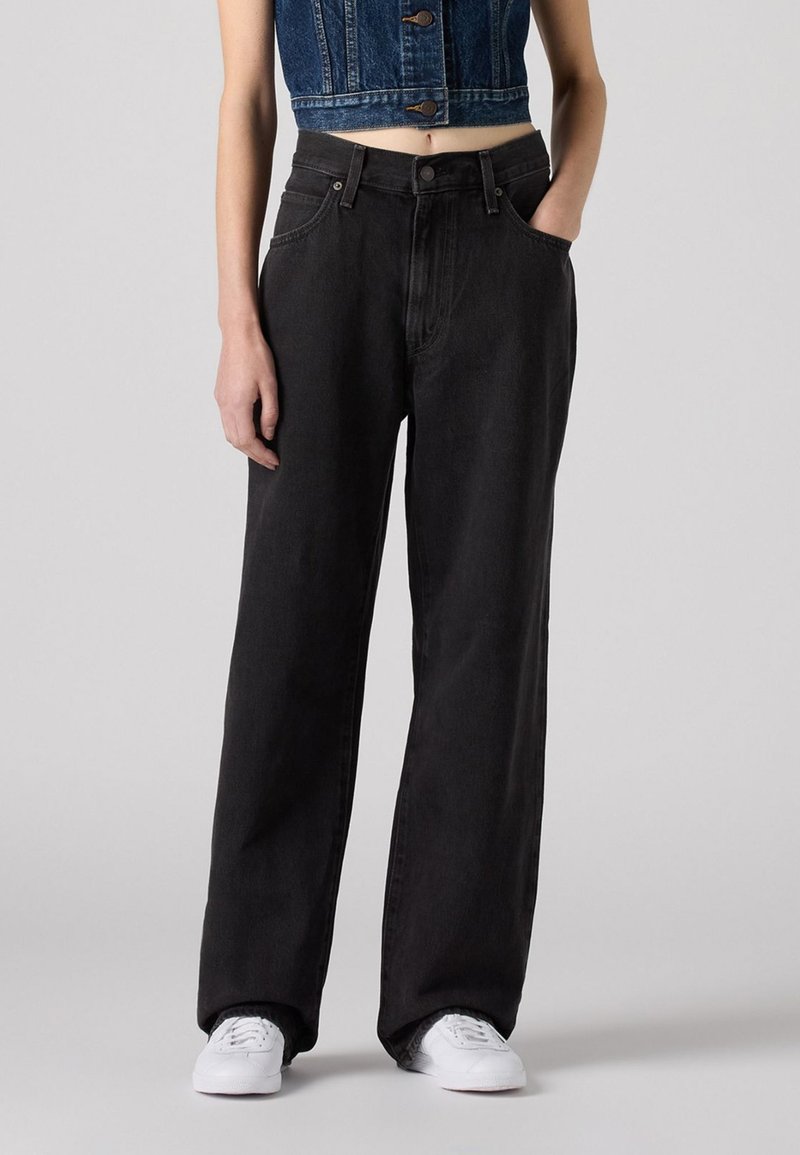Jean large noir à taille haute, en denim. Doté d'un design classique à cinq poches et de coutures contrastées. Associé à des baskets blanches.