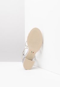 Sandalo argento con suola piatta, caratterizzato da una trama intrecciata, cinturino alla caviglia e una suola beige liscia contrassegnata da marchio e misura 37.