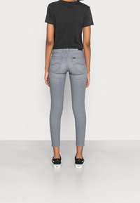 Jeans skinny grises con cintura alta, fabricados en mezcla de algodón, diseño de cinco bolsillos y detalles de costura sutiles, combinados con una camiseta negra y zapatillas.