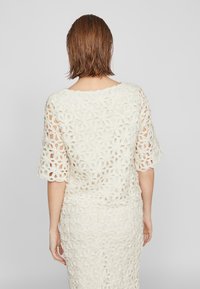 Lace heklede topp med korte ermer og blomstermønster, i off-white. Teksturlignende stoff med en avslappet passform, kombinert med et matchende skjørt.