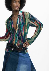 Cardigan multicolor cu un design tricotat texturat, în tonuri de verde și albastru, cu un guler contrastant. Asortat cu o fustă din denim și curele.