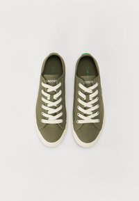 Baskets en toile vert olive avec des lacets blancs, dotées d'un dessus texturé et d'un logo subtil sur le côté. Semelles en caoutchouc avec des accents contrastants.