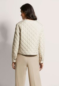 Beige gewatteerde jas met een cropped ontwerp, ronde halslijn en knoopmanchetten, gecombineerd met lichtbeige op maat gemaakte broek.