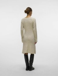 Stickad klänning i ljusbeige med ribbad textur, långa ärmar och en lätt utställd fåll, som bärs tillsammans med svarta knähöga stövlar.