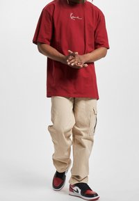 Rotes, übergroßes T-Shirt mit Weißem Logo, kombiniert mit beigen Cargo-Hosen mit Taschen und schwarz-roten Sneakers.