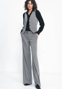 Szary kamizelka w wzór houndstooth z czarnymi guzikami, w zestawieniu z czarną koszulą i szerokimi szarymi spodniami, charakteryzującymi się gładkimi teksturami i wyraźnymi liniami.