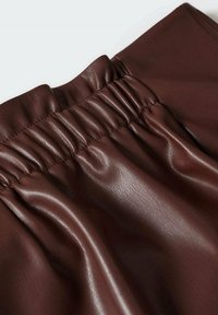 Gros plan sur une jupe en cuir marron foncé montrant une ceinture élastique froncée et une texture lisse sur un fond clair.