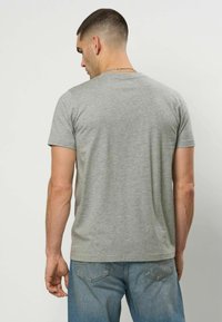 Grå t-skjorte med korte ermer og rund hals, laget av mykt bomullsmateriale. Vist bakfra, kombinert med lyseblå jeans.