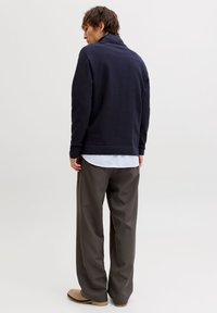 Μπλε πουλόβερ με γιακά, απαλό ύφασμα, φορεμένο πάνω από λευκό πουκάμισο. Γκρι φαρδιά παντελόνια, μπεζ παπούτσια. Μινιμαλιστικός σχεδιασμός, μονόχρωμο φόντο.