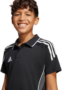 Polo shirt nera con accenti bianchi, dotata di colletto classico, maniche corte e tre strisce bianche sulle spalle.