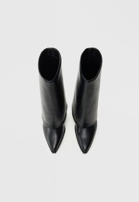 Μαύρες δερμάτινες μπότες μέχρι το γόνατο με μυτερές μύτες και λεία υφή. Διαθέτουν εφαρμοστό σχήμα και μινιμαλιστικό σχεδιασμό.