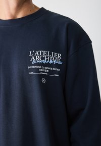 Dunkelblaues Sweatshirt aus Baumwolle mit Rundhalsausschnitt und bedrucktem weißen und hellblauen Text auf der Vorderseite. Schlichtes Design.