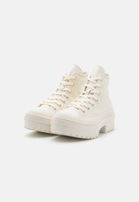 Sneakers bianchi alte realizzate in pelle liscia con una suola in gomma spessa, dotate di lace-up frontale e un sottile motivo testurizzato.