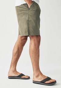 Oliven grønne shorts med sidelommer, lige snit og en glat tekstur. Båret med sorte flip-flops med en polstret sål.