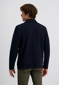 Navyblaues Langarmhemd mit Kragen, aus strukturiertem Stoff, geradem Schnitt und Rückenpasse. Kombiniert mit olivgrünen Hosen.