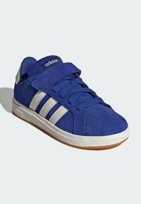 Blå mockaskor med vita ränder, rund tå, snörning och kardborrestängning, gummisula och vadderad krage för stöd.