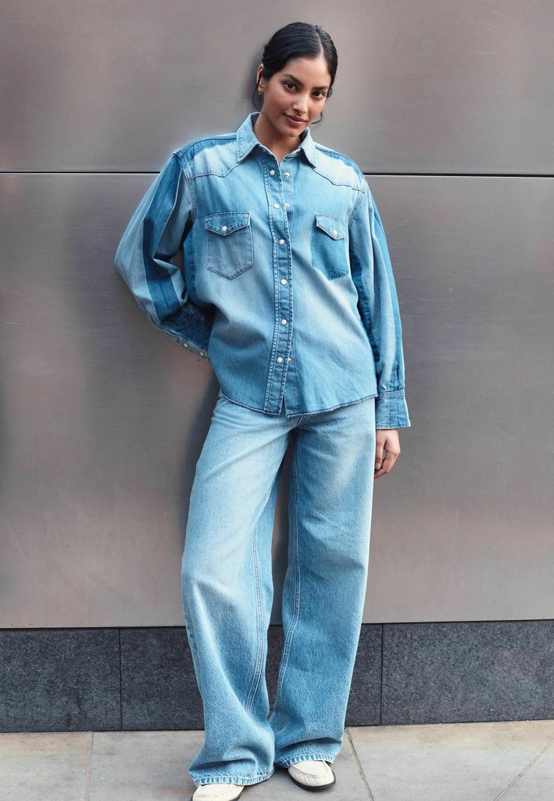 Camicia di jeans azzurri chiari con due tasche sul petto, design con bottoni, vestibilità rilassata; abbinata a jeans ampi azzurri chiari, tessuto testurizzato.
