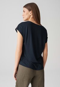 Granatowa bluzka z krótkim rękawem o luźnym kroju i okrągłym dekolcie, wykonana z gładkiego materiału, z rozcięciami po bokach u dołu.