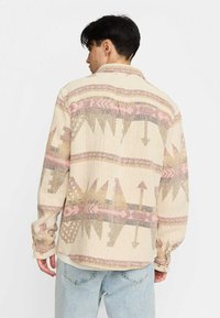 Beige gewebtes Hemd mit mehrfarbigen geometrischen Mustern, mit einem Button-Down-Kragen und langen Ärmeln. Subtile Textur im gesamten Hemd.