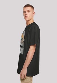 Camiseta de algodón negra con impresión gráfica de un personaje en una cápsula, con cuello redondo y mangas cortas.