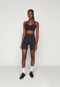 Fekete sportmelltartó és magas derekú sort, mindkettő sima textúrájú. Kicsi logóval díszítve. Fekete tornacipővel és fehér zoknival viselve.