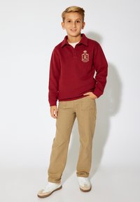 Maroone langærmet polo med krave og logo, parret med khaki cargo bukser. Hvide sneakers med beige detaljer fuldender outfittet.