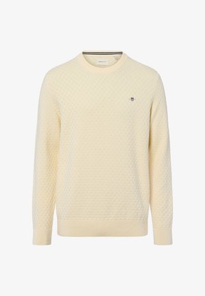 Crème-kleurige trui met een gestructureerd honingraatpatroon, ronde hals, ribbels aan de mouwen en onderkant, en voorzien van een klein geborduurd logo op de borst.