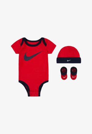 Roter Baumwoll-Overall mit schwarzem Besatz und Nike-Logo, kombiniert mit einer passenden roten Mütze und roten Stiefeln mit schwarzen Akzenten.
