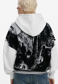 Hættetrøje med hvid hætte og sort grafisk design med abstrakte mønstre. Fremstillet af blødt stof med ribbede manchetter og kant.