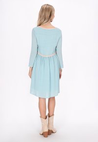Rochie lungă, de culoare albastru deschis, cu mâneci lungi, cu talie strânsă și un finisaj texturat. Prezintă un accent contrastant de culoare roz la gât și la talie.