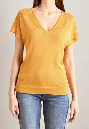 Gul strikket kortærmet sweater med V-hals og diamantmønster på skuldrene. Glat tekstur, ribbet kant og løs pasform.