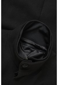 Svart ullblandad jacka med hög krage och en smidig innerfoder. Utrustad med knappstängning och en ficka med dragkedja inuti.